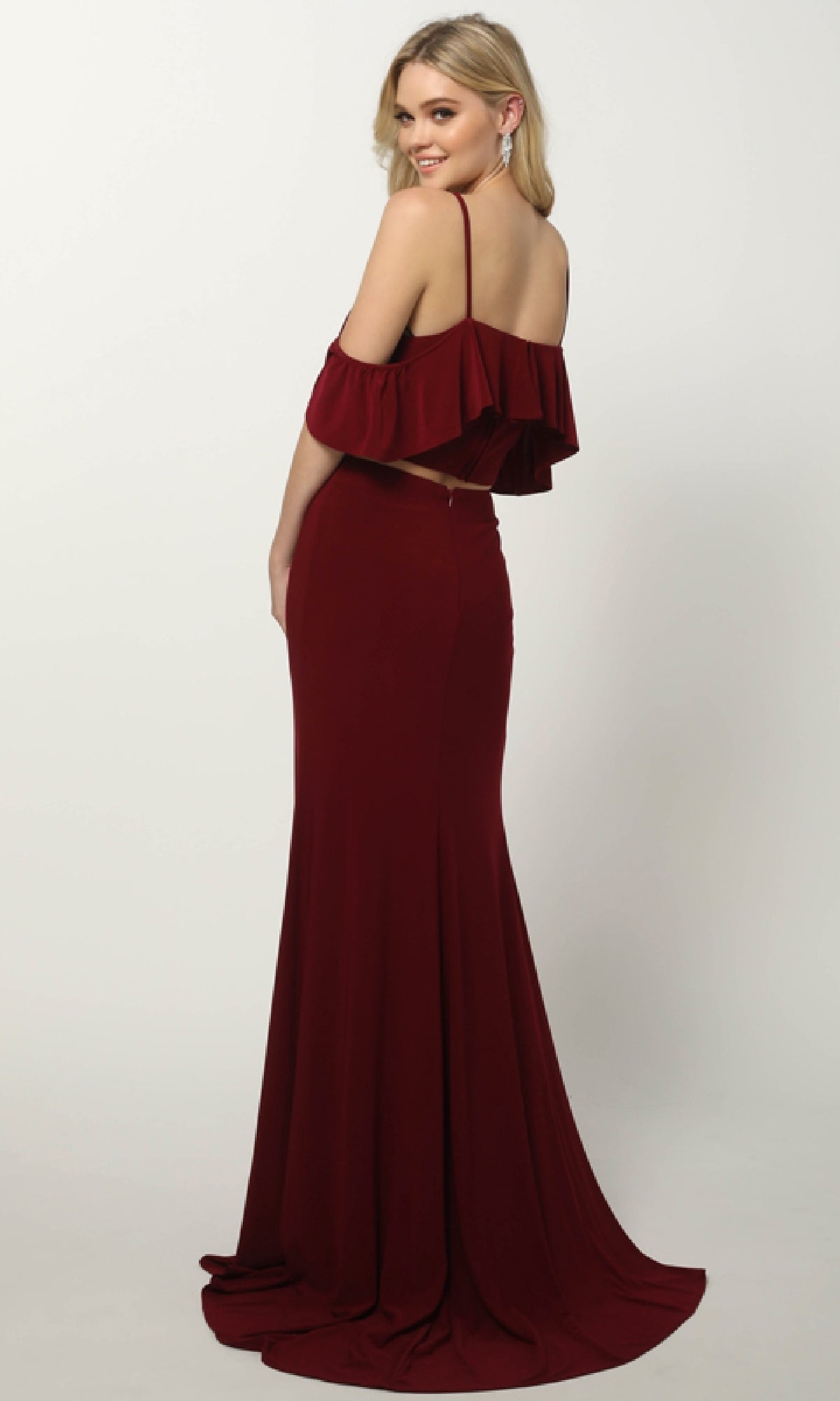 Woman posing elegantly in the Juliet 662 long prom dress, a burgundy two-piece with a ruffled off-shoulder top and floor-length skirt, set against a plain light background.